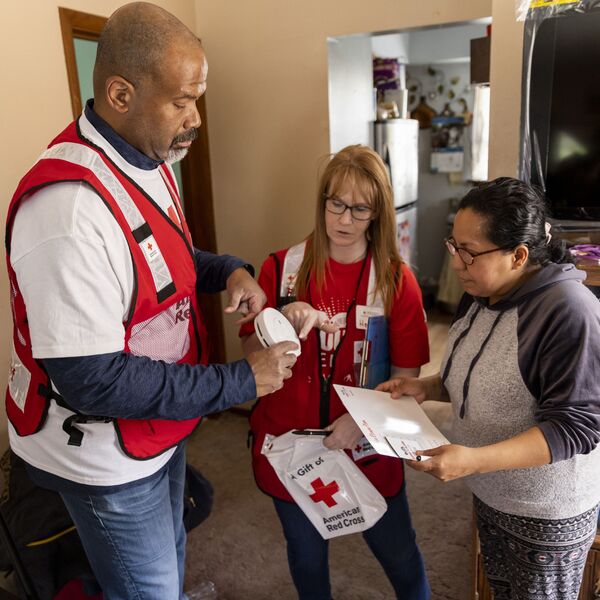 April 29, 2023. Omaha, Nebraska. American Red Cross volunteers James Boles and Heidi Briggs show resident Blanca Gijon the free smoke alarms they are installing in her home as part of a Sound the Alarm event in Omaha, Nebraska. “At this age, I really want most of what I am doing to be beneficial and add up to something good for people, and the Red Cross provides a unique opportunity for that,” James said. Photo by Scott Dalton/American Red Cross